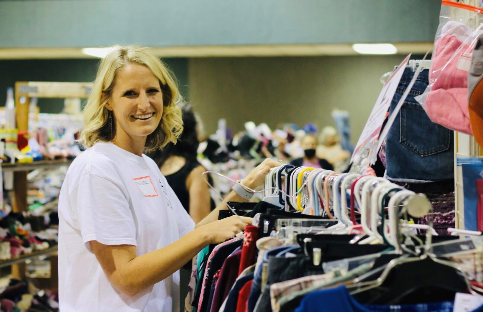 A smiling Team Member stands behind a rack of toddler girl's clothing at the sale.